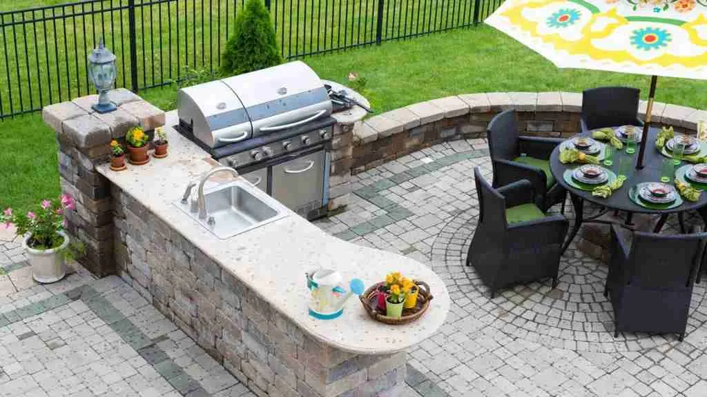 Outdoor kitchen with a stone island, sink, grill, and furnished backyard patio