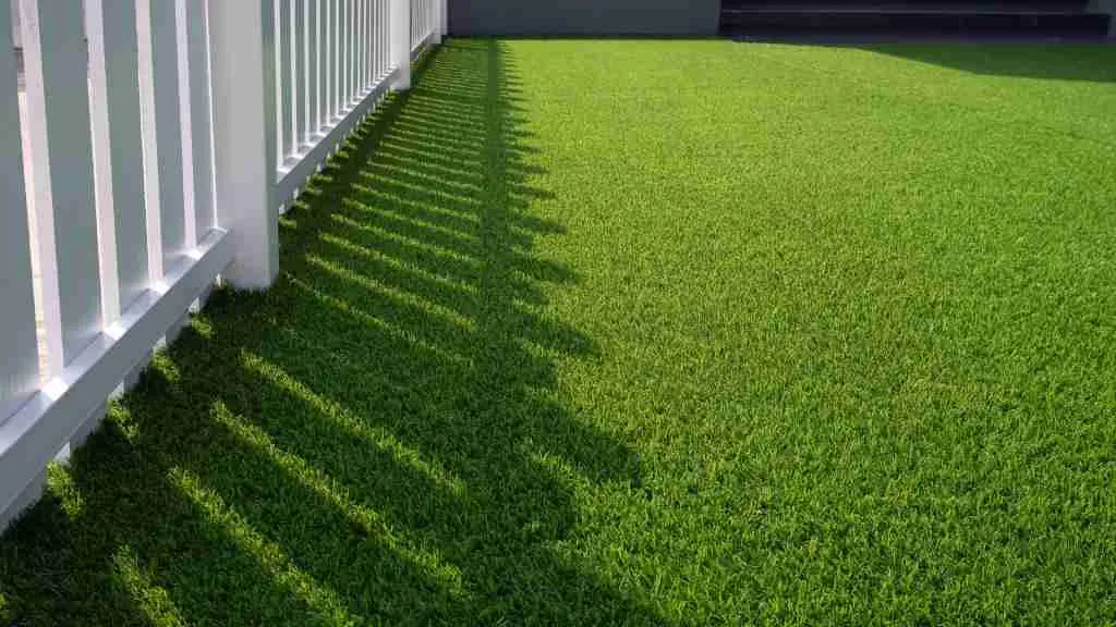Artificial grass installation in a backyard with clean white fencing